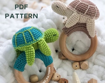 May include: Two crochet turtle baby rattles. One turtle is teal and green, the other is beige and brown. Each turtle is attached to a wooden ring. The text "PDF PATTERN" is in the upper left corner. The text "@crochetstreet_pattern" is on the wooden ring.