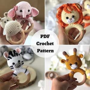 May include: A set of four crochet animal rattle toys. The toys are a pink elephant, a brown hippo, a black and white zebra, and a yellow giraffe. Each toy is attached to a wooden ring.