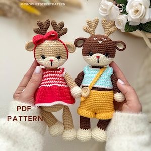 May include: Two handmade crochet deer dolls. One wears a red and white striped dress and a red bow. The other wears a blue shirt and yellow shorts. Both have brown antlers and are held by hands. The text "PDF PATTERN" is visible.