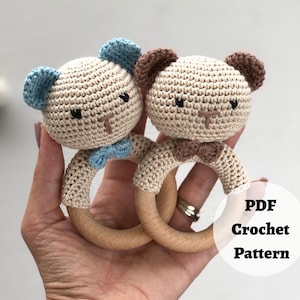 May include: A crochet pattern for two bear rattle toys. The bears are beige with brown ears and blue or brown bow ties. The rattles are made with wooden rings.