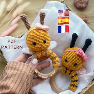 Può includere: Due giocattoli a forma di ape in crochet con anelli di legno. Le api sono gialle e marroni con accenti rosa. I giocattoli sono perfetti per neonati e bambini piccoli.