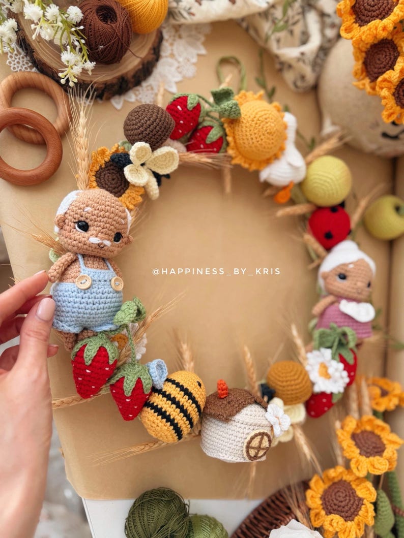 K&ouml;nnte beinhalten: Ein runder H&auml;kelkranz mit zwei kleinen Puppen, einer Biene, einem Haus, Erdbeeren, Sonnenblumen und Weizen&auml;hren. Der Kranz ist mit verschiedenen Elementen aus Garn verziert und enth&auml;lt den Text @HAPPINESS_BY_KRIS in der Mitte.