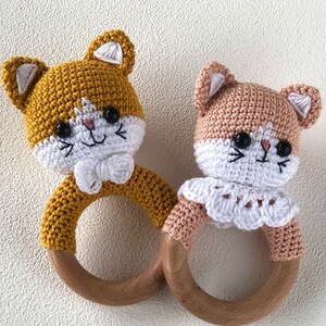 May include: Two crocheted cat rattle toys with wooden rings. One is yellow and the other is peach.