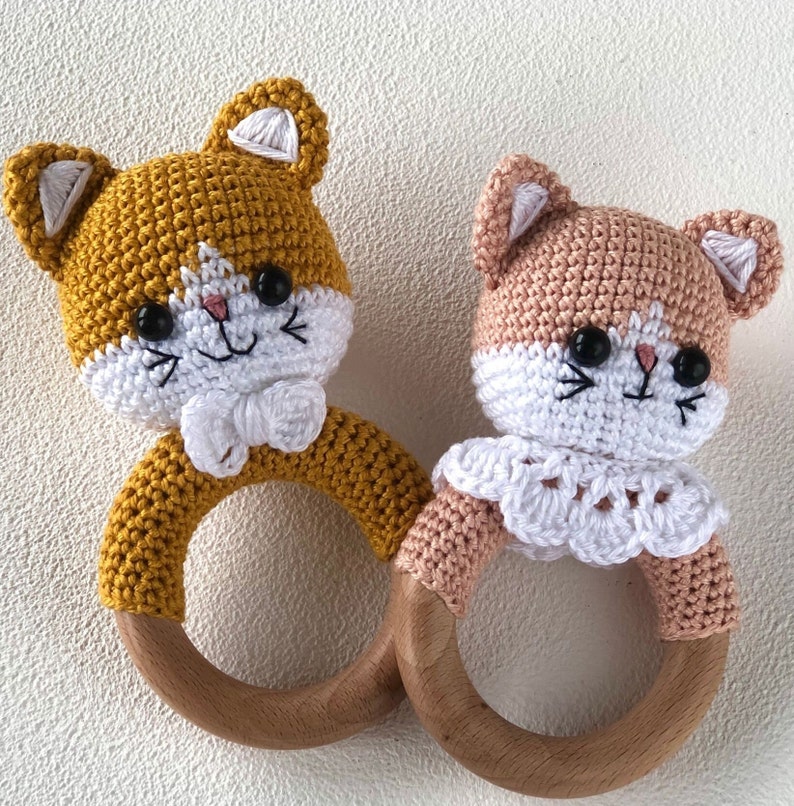 May include: Two crocheted cat rattle toys with wooden rings. One is yellow and the other is peach.