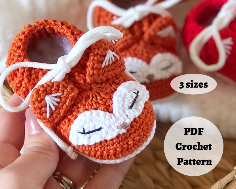 May include: Orange and white crocheted baby booties with a fox face design. The booties have white laces and are available in three sizes. PDF crochet pattern.