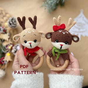 May include: Two crocheted reindeer rattle toys with wooden rings. One reindeer is brown with a green scarf and the other is beige with a red scarf. The text "PDF PATTERN" and "@CROCHETSTREETPATTERN" is visible in the image.