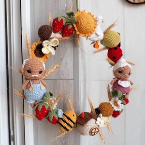 K&ouml;nnte beinhalten: Ein runder Kranz, der mit verschiedenen geh&auml;kelten Figuren verziert ist, darunter ein &auml;lteres Paar, eine Biene, eine wei&szlig;e Ente, ein Marienk&auml;fer, Erdbeeren, Sonnenblumen, Pilze und Weizen&auml;hren. Die Figuren sind rund um den Rahmen angeordnet.