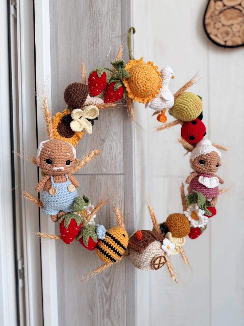 K&ouml;nnte beinhalten: Ein runder Kranz, der mit verschiedenen geh&auml;kelten Figuren verziert ist, darunter ein &auml;lteres Paar, eine Biene, eine wei&szlig;e Ente, ein Marienk&auml;fer, Erdbeeren, Sonnenblumen, Pilze und Weizen&auml;hren. Die Figuren sind rund um den Rahmen angeordnet.