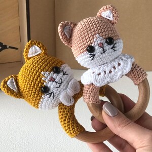 May include: Two crocheted cat rattle toys with wooden rings. One cat is yellow and the other is light brown. Both have white crocheted collars.