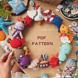 May include: A circular arrangement of various crocheted sea-themed figures including a crab, octopus, seahorse, starfish, sailboat, and lifebuoy, surrounding the text PDF PATTERN and @HAPPINESS_BY_KRIS on a plain background.