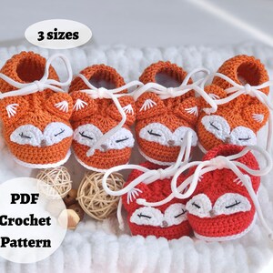 May include: Three pairs of crocheted baby booties in orange and white, featuring a fox face design. The booties have white laces and are arranged in a white basket. The text "3 sizes" and "PDF Crochet Pattern" are visible in the image.