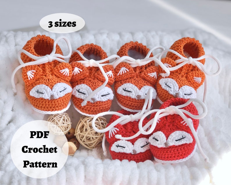 May include: Three pairs of crocheted baby booties in orange and white, featuring a fox face design. The booties have white laces and are arranged in a white basket. The text "3 sizes" and "PDF Crochet Pattern" are visible in the image.