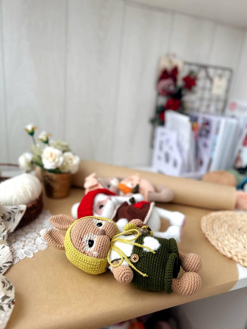 May include: A crocheted bunny toy wearing a green and white outfit and a yellow hat. The bunny is lying on a brown surface.