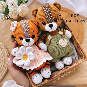 Puede incluir: Dos peluches de tigre de crochet, uno con un vestido melocotón con una flor blanca y el otro con un mono verde con un corazón. Los peluches están sentados en una cesta de mimbre. El texto "PDF PATTERN" está en la esquina superior derecha de la imagen.