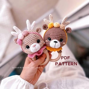 May include: Two crocheted deer rattle toys with wooden rings. One deer is brown with yellow accents and the other is brown with pink accents. The text "PDF PATTERN" is visible in the image.