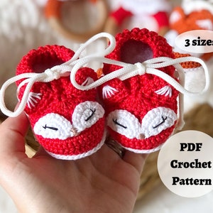May include: Red crocheted baby booties with white fox faces and white laces. The booties are in a hand. The text "3 sizes" and "PDF Crochet Pattern" is on the image.