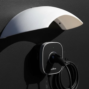May include: A white, curved wall-mounted electric vehicle charger with a black charging unit and cable. The charger has a sleek, modern design, with the brand name "wallbox" visible on the unit.