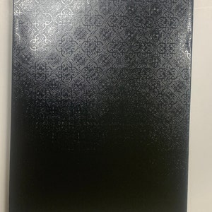 May include: A rectangular, black object with a textured surface. The top portion features a silver, ornate pattern, while the bottom half is a solid black. The object appears to be a box or a similar container.