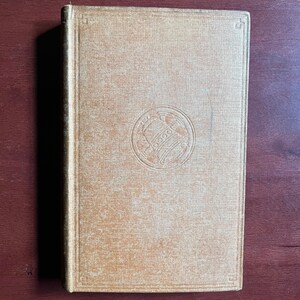 May include: A tan hardback book with a decorative circle design on the front cover.