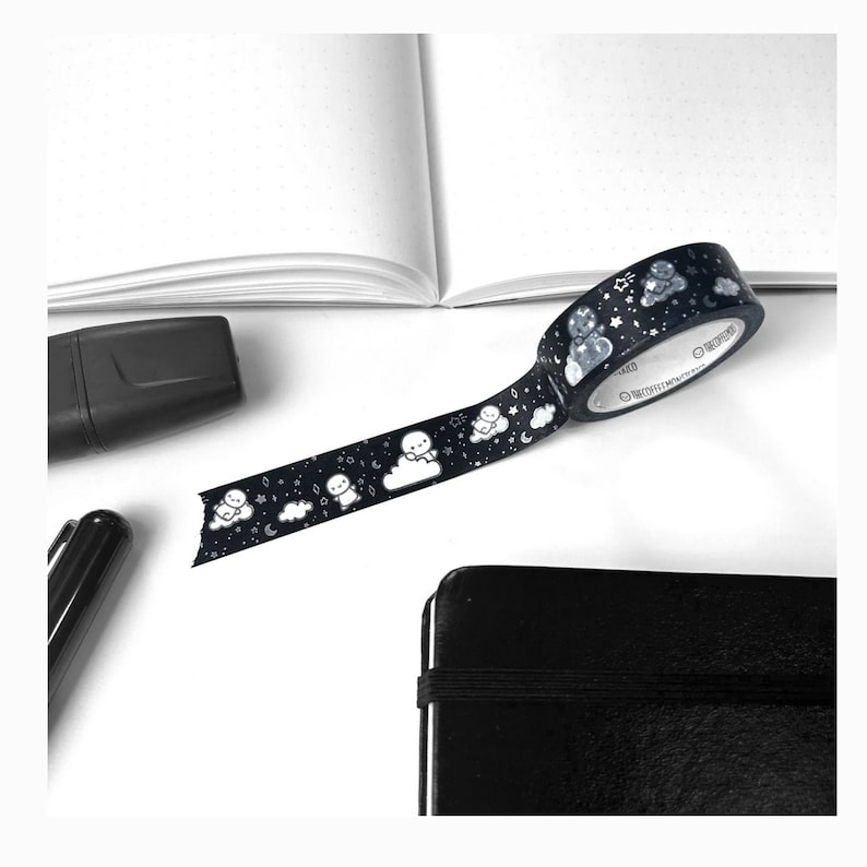 May include: Black and white washi tape with a repeating pattern of clouds and small figures. The tape is rolled up and partially unrolled on a white surface.