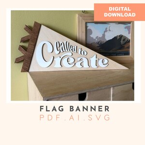 May include: A wooden flag banner with the text "Called to Create" in white letters. The banner is a triangular shape with a brown wooden top. The banner is sitting on a wooden shelf.