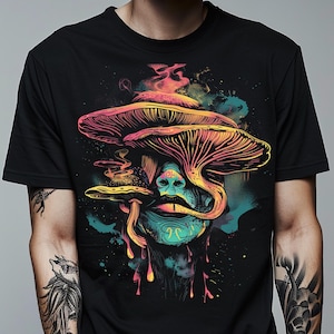 Puede incluir: Camiseta negra con un gráfico colorido de una cara fusionada con setas. El diseño utiliza tonos de rosa, amarillo, azul y verde, creando un efecto psicodélico. La obra de arte tiene un estilo ilustrativo detallado.