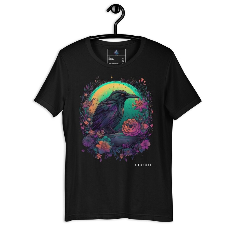May include: Black t-shirt with a graphic of a crow sitting on a branch surrounded by flowers. The crow is black with a green and purple glow. The flowers are pink, purple, and blue. The text "KAMIBJI" is at the bottom of the design.