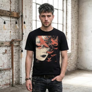 K&ouml;nnte beinhalten: Schwarzes T-Shirt mit einem k&uuml;nstlerischen Design eines Frauengesichts und roten V&ouml;geln. Die Grafik befindet sich auf der Vorderseite des T-Shirts. Das Model tr&auml;gt ein braunes Lederarmband und blaue Jeans.