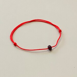 May include: A red string bracelet with a small, dark red bead.