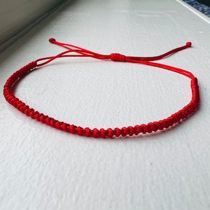Peut inclure: Un bracelet rouge en cordon avec un motif noué. Le bracelet est noué avec un nœud coulissant pour un ajustement facile.