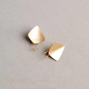 Puede incluir: Un par de pendientes de color dorado con un diseño geométrico en forma de diamante. Los pendientes tienen un acabado liso y pulido.