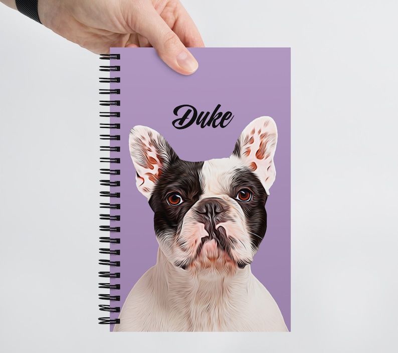 May include: A purple spiral bound notebook with a white and black French bulldog illustration and the name "Duke" printed in black.
