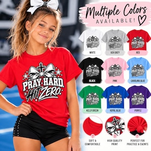 Könnte beinhalten: Ein rotes Kurzarm-T-Shirt mit einem Grafikdruck einer großen Schleife, einem Kreuz und dem Text PRAY HARD HIT ZERO. Das Bild zeigt mehrere Farboptionen, darunter Weiß, Aschgrau, Rot, Schwarz, Pink, Blau, Grün und Lila.