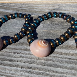 May include: Four bracelets with blue and gold beads and a shell charm. The shells are a light brown color with a spiral pattern.