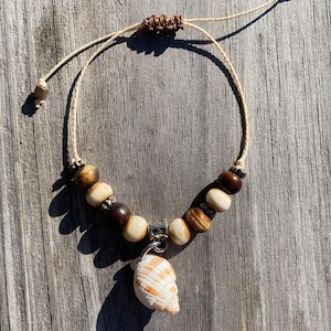 May include: A white cord bracelet with brown and white beads and a seashell charm.