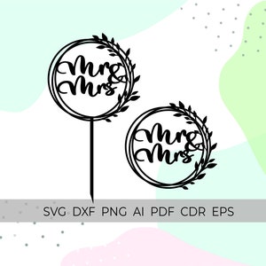 May include: Black laser-cut cake topper with the words "Mrs & Mrs" inside a circular frame, adorned with a leafy wreath design. The topper has a long stem for insertion into a cake. The image also includes a smaller version of the topper.