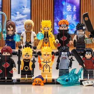 May include: A collection of fifteen Naruto-themed minifigures featuring various characters in signature outfits, including capes, headbands, and accessories like swords, scrolls, and a translucent blue shark figure, all standing on individual black bases.