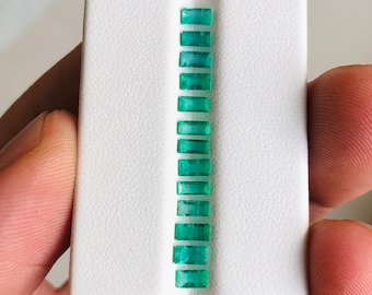 May include: A white card with a row of emerald green rectangular gemstones.