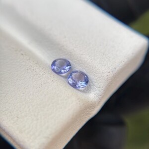 May include: Two small, round, purple gemstones on a white surface.