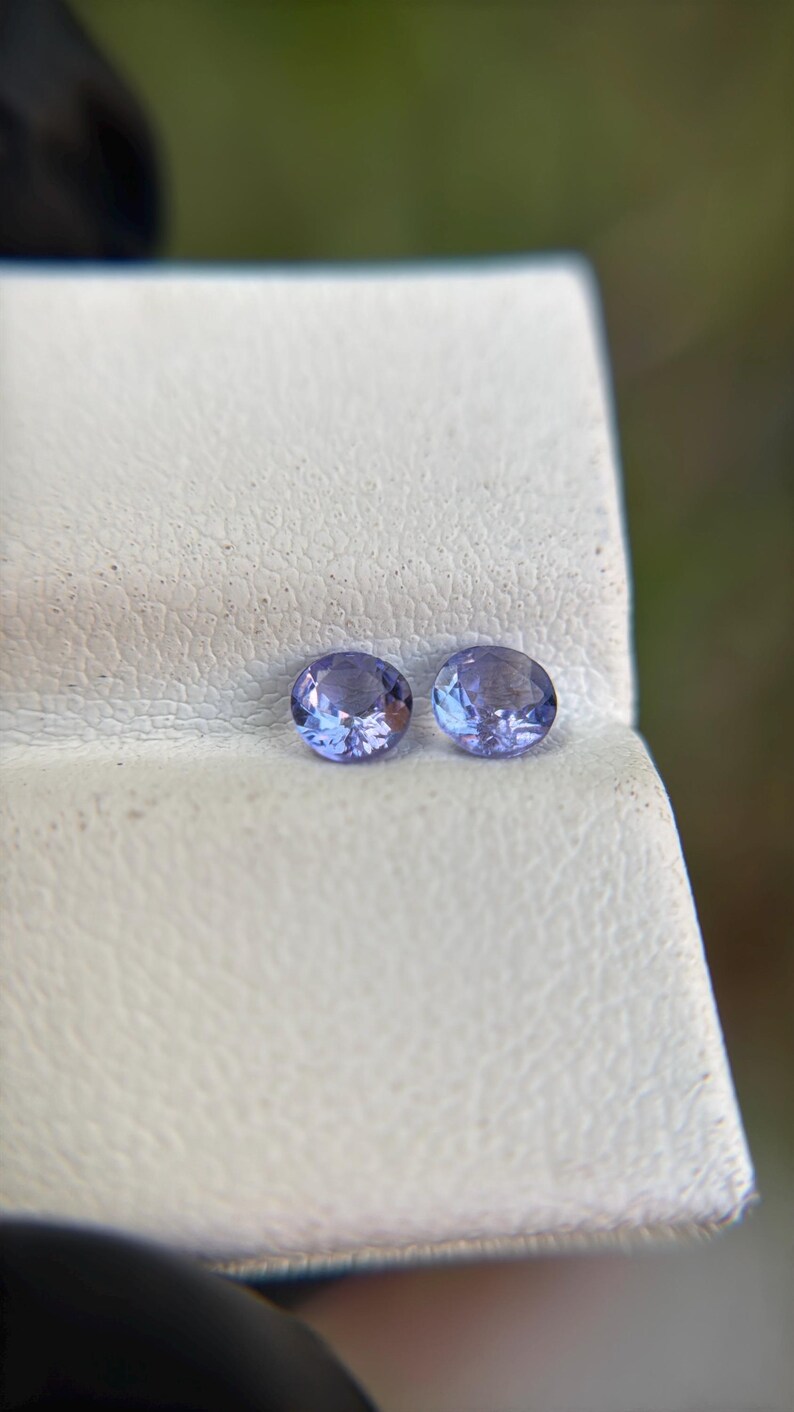 May include: Two round, purple gemstones on a white surface.