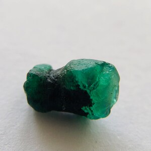 May include: A dark green emerald crystal with a rough, natural texture. The crystal is a deep green color and has a slightly translucent appearance.