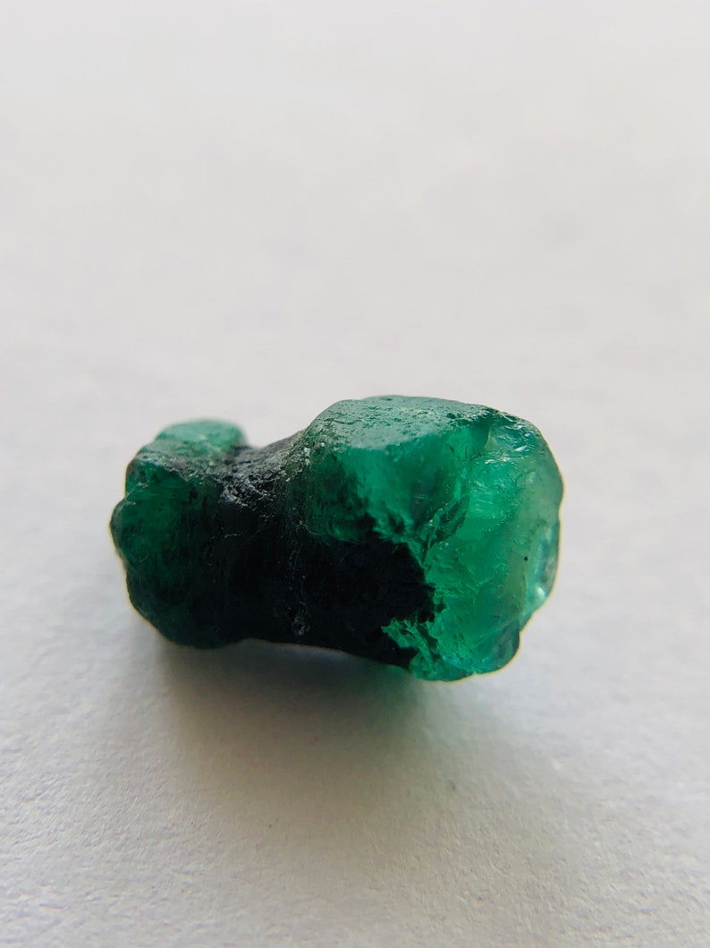 May include: A dark green emerald crystal with a rough, natural texture. The crystal is a deep green color and has a slightly translucent appearance.