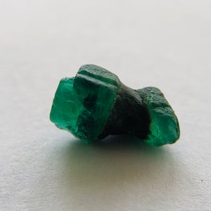 May include: A dark green emerald crystal with a rough, faceted surface. The crystal is a deep green color and has a natural, unpolished look.