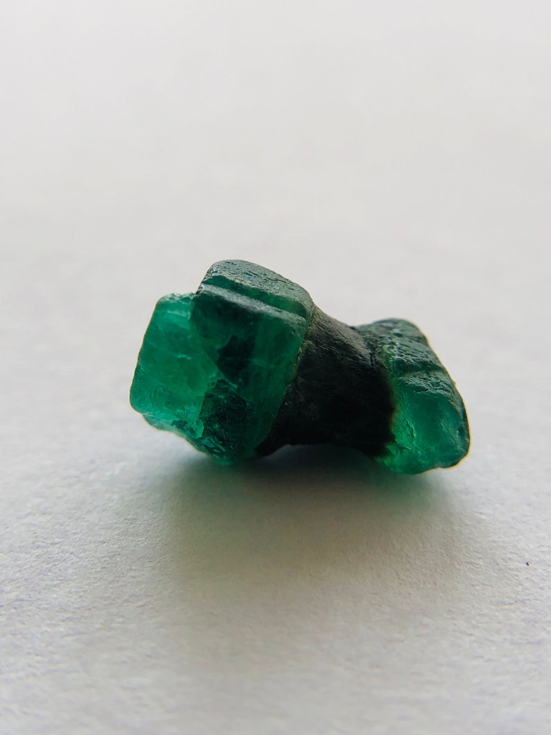 May include: A dark green emerald crystal with a rough, faceted surface. The crystal is a deep green color and has a natural, unpolished look.