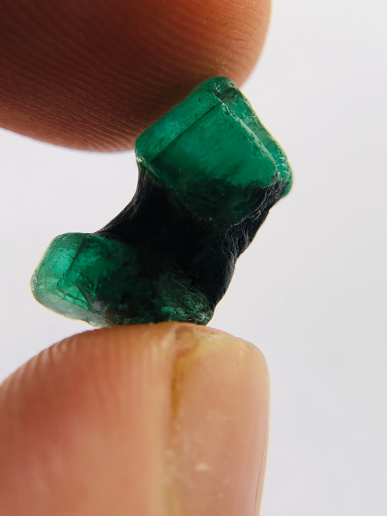 May include: A dark green emerald crystal with a rough, natural texture. The crystal is shaped like a small, irregular block.