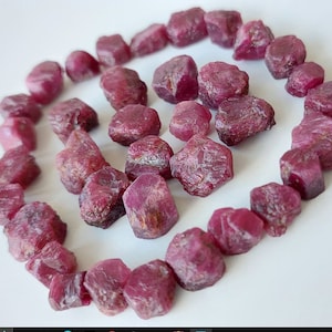 以下が含まれることがあります： ルースの原石ルビーの集まり。ルビーは濃いピンク色で、形やサイズが様々です。