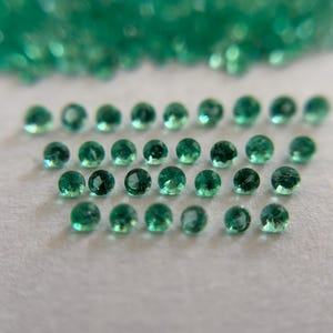 May include: A collection of small, round, faceted emerald green gemstones arranged in rows. Each stone features a brilliant cut with multiple reflective surfaces, displaying a deep, vibrant green hue throughout the entire set of loose gems.
