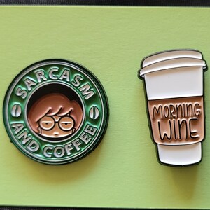 May include: Two enamel pins. One is green and features a cartoon woman with the text "Sarcasm and Coffee". The other is white and features a coffee cup with the text "Morning Wine".