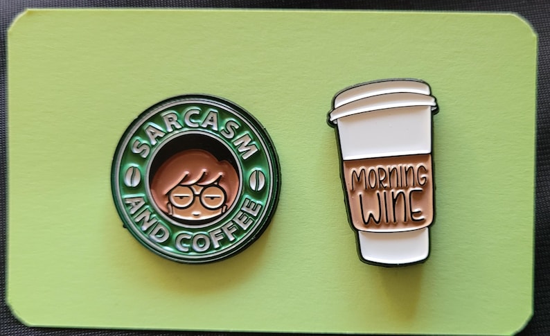 May include: Two enamel pins. One is green and features a cartoon woman with the text "Sarcasm and Coffee". The other is white and features a coffee cup with the text "Morning Wine".
