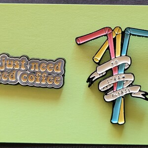 May include: Two enamel pins. One pin says "I just need iced coffee" in a retro font. The other pin features three colorful straws with a white banner that says "No Straw Please".